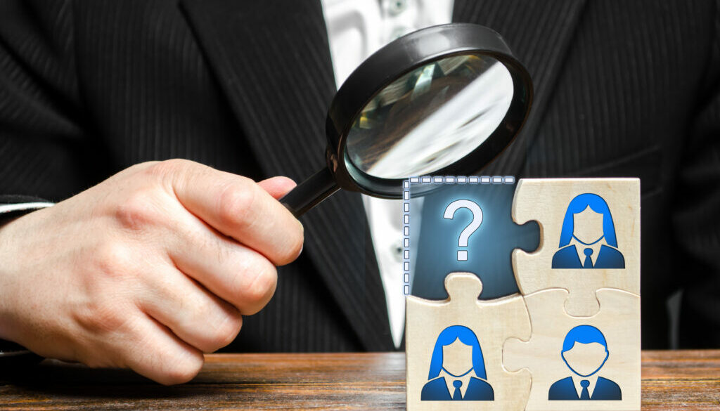 Businessman with a magnifying glass examines the missing part of the puzzle team. Search, recruitment staff, hiring leader. Creating an effective business team. Lack of specialists in the labor market